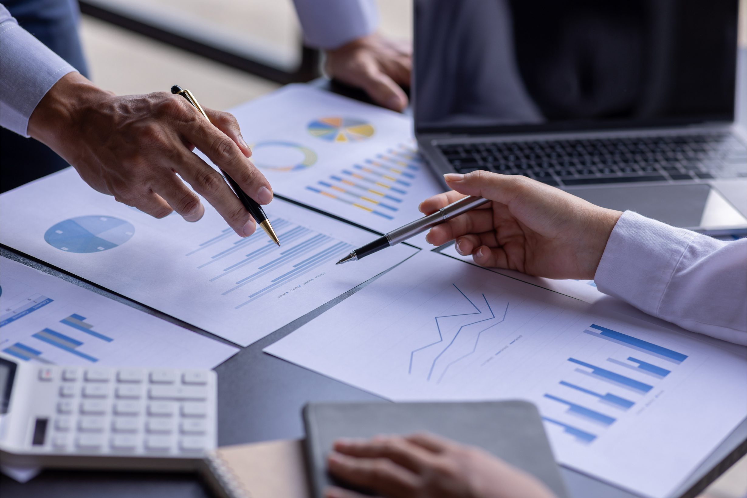 Hands analyzing charts and graphs on desk.