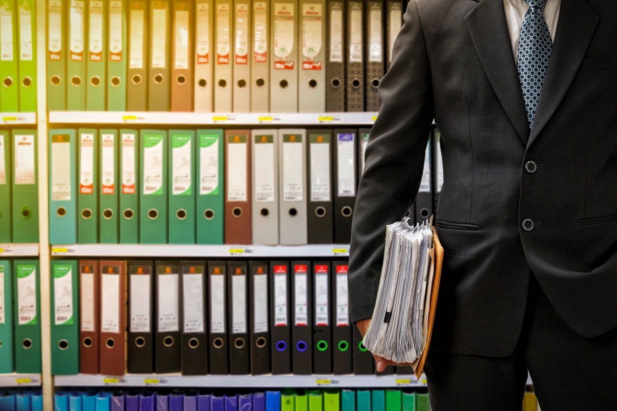 Businessman holding a briefcase standing by shelves of organized binders.